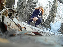 Ginger bridesmaid makes water behind a tree in the forest